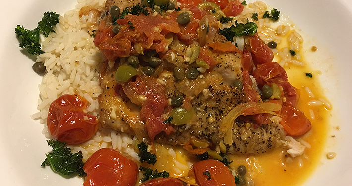 A blackened fish fillet over rice, covered with a chunky tomato and sweet pepper sauce.
