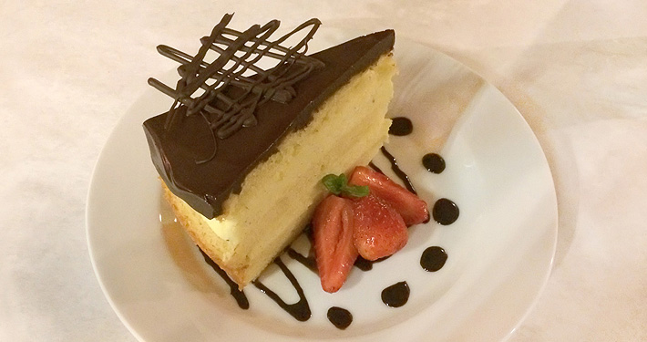 A wedge of cheesecake finished with a lattice of dark chocolate and dots of sauce on the plate.