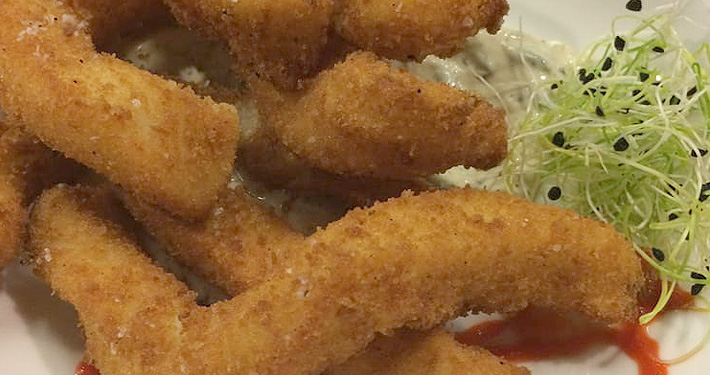 A pile of long, breadcrumbed eggplant fries fried golden and stacked on a white plate.