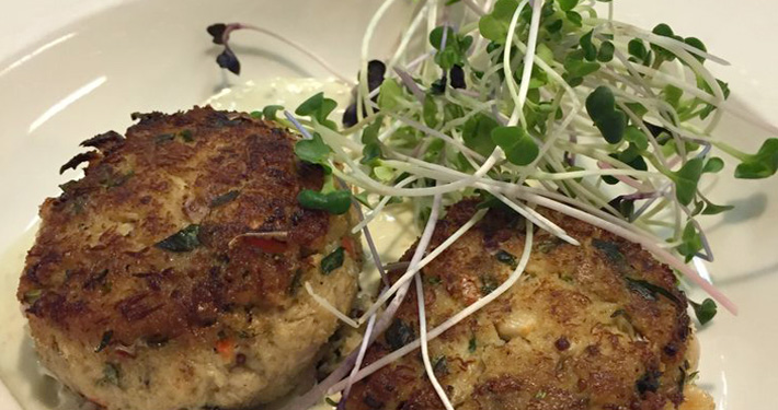 Two golden crab cakes topped with a tangle of micro sprouts.
