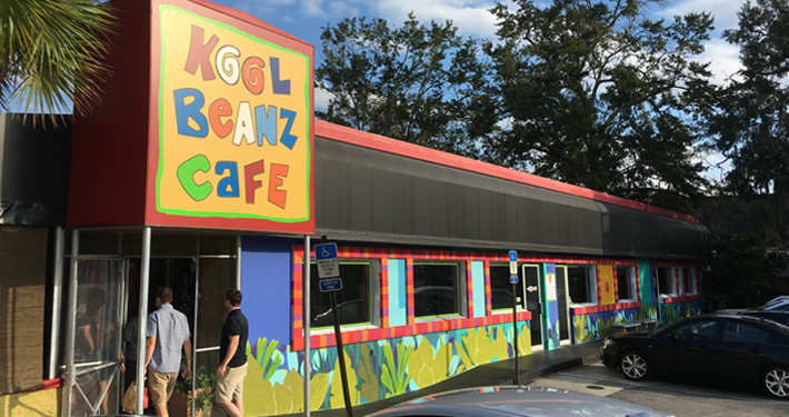 Kool Beanz Cafe seen from across the road, with people walking past the painted storefront.