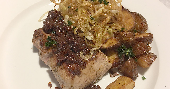 A seared and sliced pork loin with fingerling potatoes and a tangle of fried shallots.