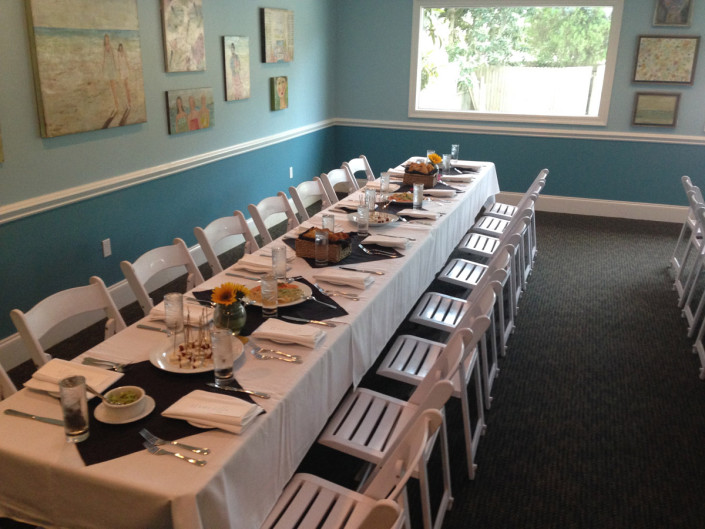 A set table in The Room with plated food and wine glasses, artwork hung along the wall behind.